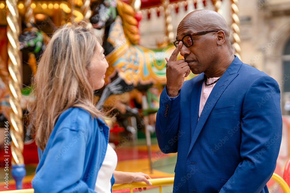 Fototapeta premium Couple talks in front of a carousel at a fairground during the daytime in a city