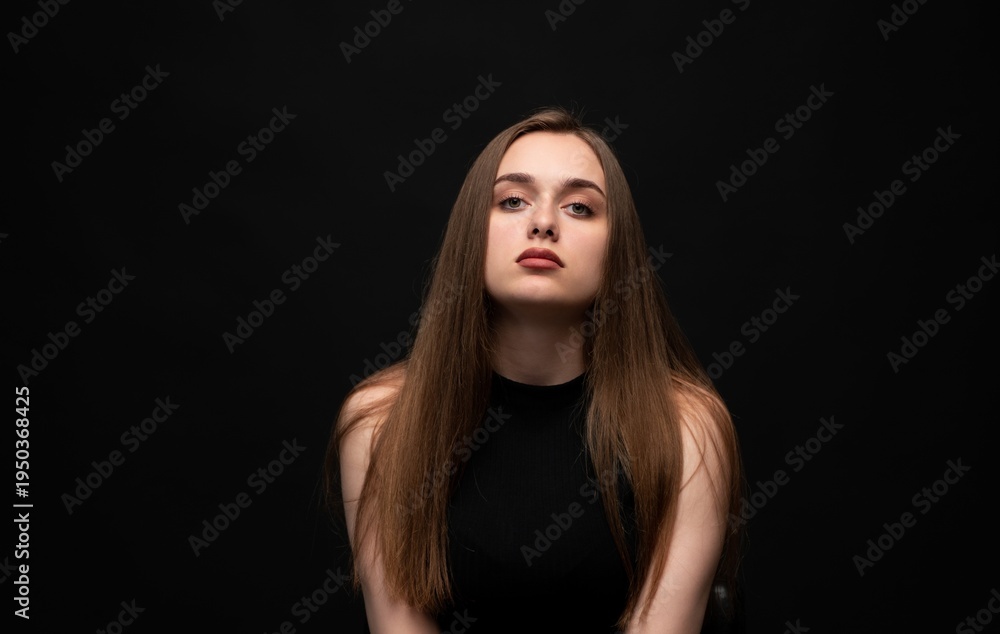 Fototapeta premium Young woman with natural long hair and serious expression posing on plain black background, portraying beauty and strength