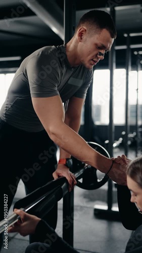 A fitness trainer supports and motivates a woman during weightlifting in a modern gym. He holds her hands, offering encouragement and ensuring proper form. determination in achieving fitness goals.