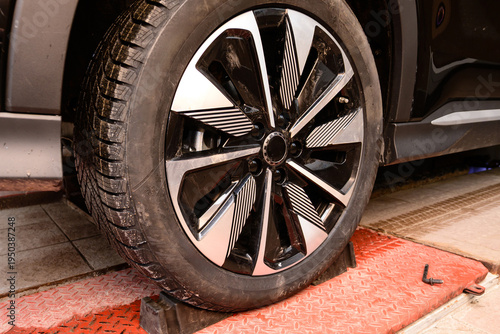 Wheel alignment and alignment on the car service platform. Car tire being repaired while on service lift in a workshop during daytime in the city center