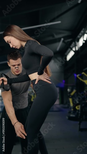 Dedicated personal trainer coaching a young woman during a challenging suspension training session in a modern gym, helping her maintain proper form and technique for optimal results. vertical