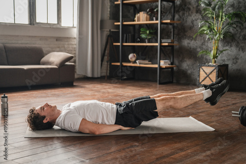 Domestic fitness success. Smiling young man lie on back on gymnastic mat at living room do core strength workout abdominal exercises swing press enjoy good result feel proud of daily discipline