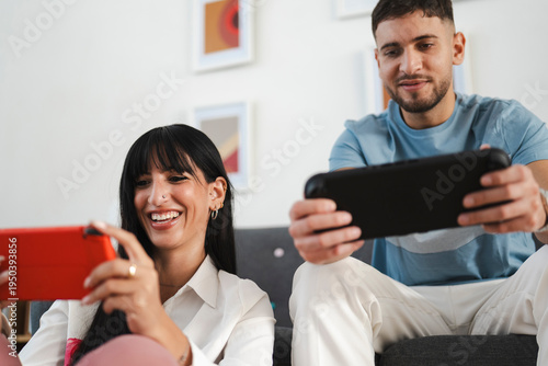 A young couple enjoys playing a video game together on a portable console in a bright, modern living room.