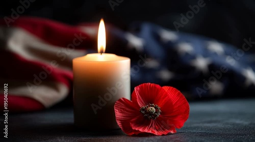 A lit candle beside a red poppy flower on a dark surface. An American flag is partially visible in the background, symbolizing remembrance and honor for fallen soldiers.