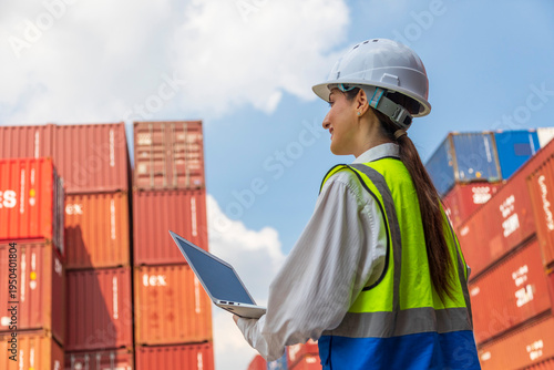 Beautiful woman officer checking container cargo and holding laptop computer checking inventory. Female staff in logistics import and export shipping business concept.