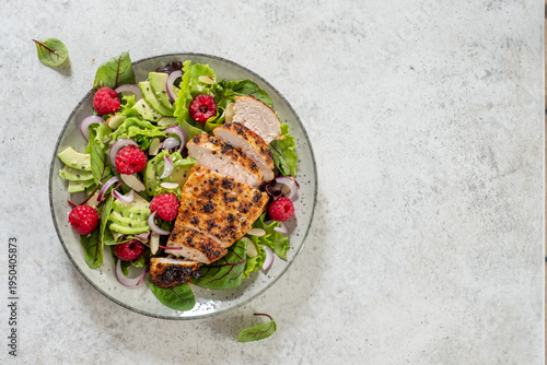 Fresh salad with grilled chicken, avocado, and raspberries served on a plate