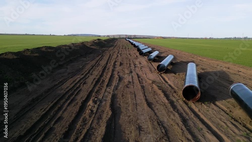 Ground-level perspective of steel pipes for the Balkan Stream gas pipeline in Bulgaria. Row of large diameter tubes on a construction site across green fields under a clear sky