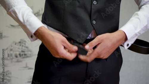Groom Man Adjusting Black leather Belt with Elegant White Shirt and Tailored Trousers.