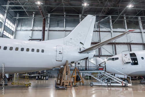 White passenger aircrafts in the airplane hangar. Planes under maintenance. Checking mechanical systems for flight operations