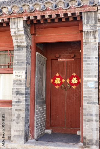 Traditional red wooden door of a classic grey brick house in a Beijing hutong alley with lucky Fu character symbols.