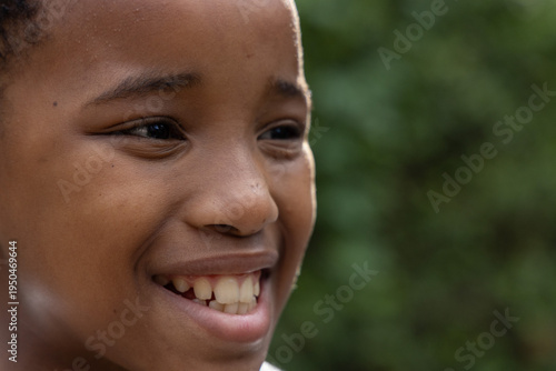 African American child boy smiling, facing right in garden, showing teeth, short hair, light collar