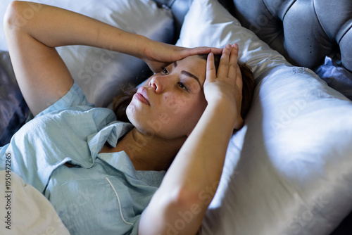 Vertical video: Reacting to soft light, woman in pjs pressing hands to temples on bed with pillows