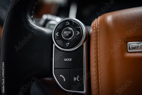 Photos Close up shows left side multifunction controls on a Range Rover wheel, with tan and black stitched leather, MENU OK pad, MODE, phone, and voice buttons in low key light