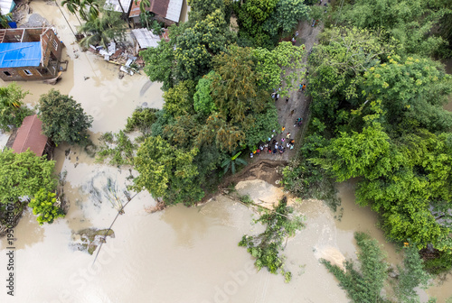 An aerial view residents gathering near a damaged rural road after flooding caused a section to collapse along a riverbank following heavy rainfall