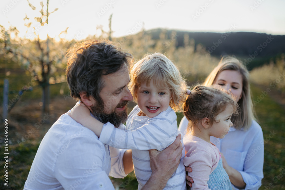 Fototapeta premium Spring portrait of parents with two small children on wlak in blooming orchard.