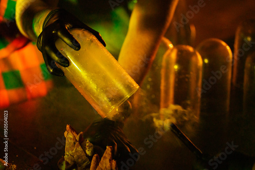 Photography A gloved hand pours a yellow liquid from a beaker over a crushed substance in a dimly lit lab