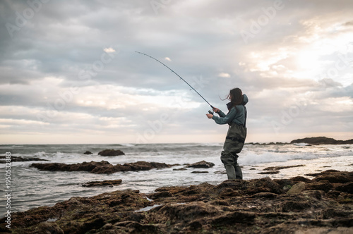 Foto Woman Catching Fish from Rocky Shore with Spinning Rod, Fishing Success, Outdoor