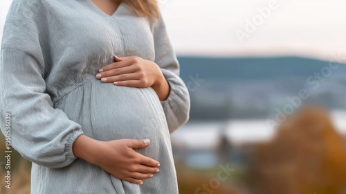 Pregnant woman gently holding her burgeoning belly with both hands, showing care and expectation of a future baby
