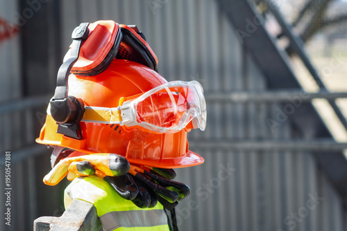 Construction safety helmet with protective goggles, ear protection and work gloves at building site. Personal protective equipment for industrial work, construction safety and workplace protection.