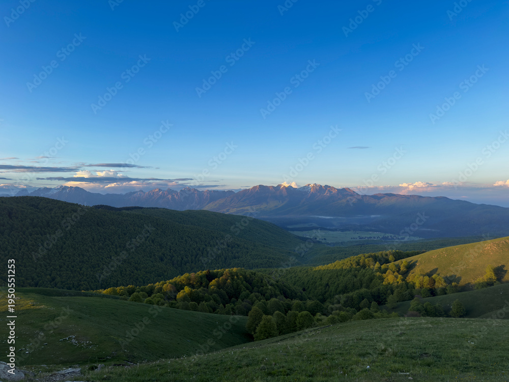 Fototapeta premium Panorama montano con valli verdi sotto cielo azzurro cristallino.
