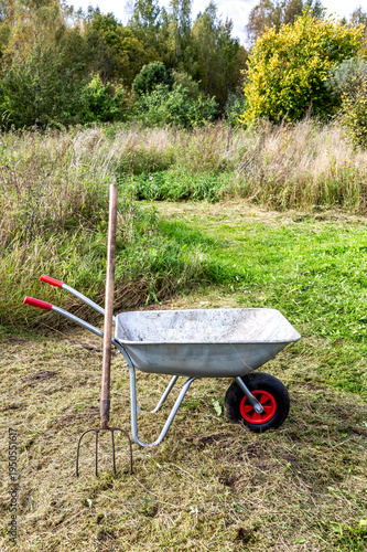 Hay is stacked on a garden cart on a summer. A pitchfork is stuck in the ground.