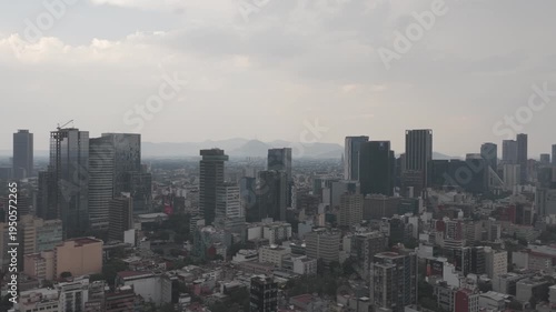 Aerial panoramic view of the Paseo de la Reforma skyline in Mexico City with modern skyscrapers, drone flying left to right under a hazy overcast sky
