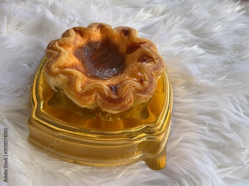 Caramel egg tart with custard filling on golden plate, baked dessert on white background
