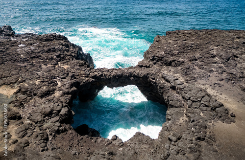 Pont Naturel, Natural stone arch on the coast of Mauritius. The turquoise Indian Ocean flows beneath the rocky arch, surrounded by rugged cliffs, creating a dramatic and picturesque coastal landscape