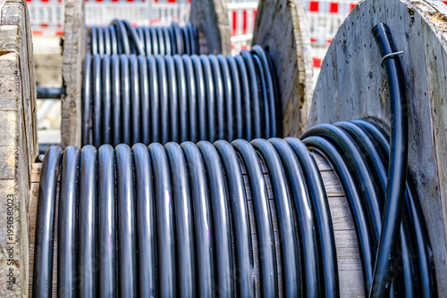 Construction work takes place near a road with bright green cable on a large spool during daytime in a city area