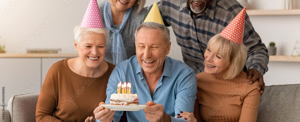 Naklejka premium Friends gather in a cozy living room to celebrate a birthday. One person holds a cake with candles. Everyone smiles and enjoys the moment together.