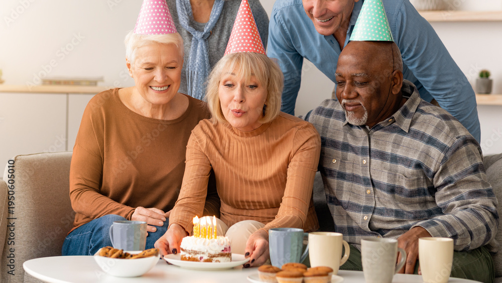 Naklejka premium A group of friends gathers in a living room to celebrate a birthday. They are smiling and enjoying cake with candles. The atmosphere is joyful and filled with friendship.