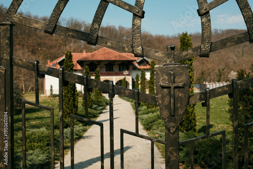 Iron gate with Christian cross leading to Ribnica Monastery courtyard near Mionica Serbia. Religious architecture representing faith spirituality pilgrimage tradition sacred heritage tourism.