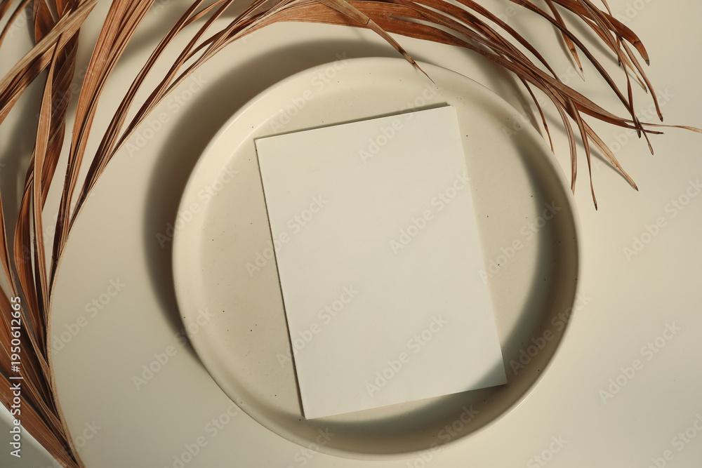 Naklejka premium Minimal Blank Card Mockup on Ceramic Plate. Dried Palm Leaves in Sunlight. Beige Table Background. Natural Neutral Branding Template, Elegant Summer Wedding Stationery Scene. Copy Space, Flatlay, top