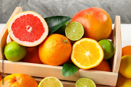 Different ripe citrus fruits in crate on table, closeup