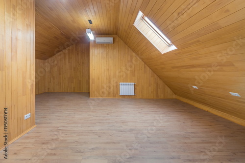 A spacious room with wooden walls and floors has a sloped ceiling. Skylights let in natural light. The space is empty and ready for furniture. It is located in a residential area