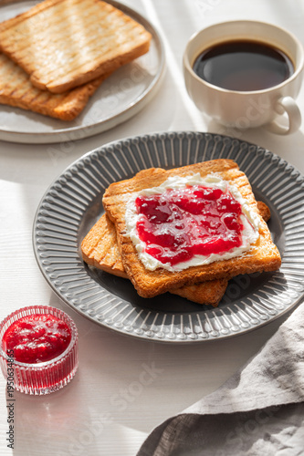 Toast with sweet berry-fruit jam and cream cheese on a plate on a white wooden background