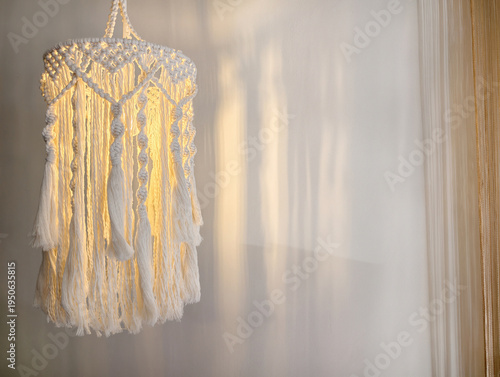 Cozy boho macrame pendant lamp glowing softly in minimalist white interior. Handcrafted tassels and intricate knots add warmth and texture to modern decor. Ideal for living room or bedroom ambiance