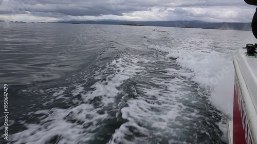 a small section of the stern of a moving vessel at sea leaving a trail of foam that visually blends with the smoke coming from the engine.