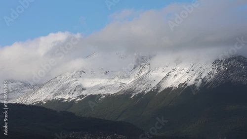 Close-up video showing a mountain range in Ushuaia covered in snow; the mountain peaks have gray clouds, but the sky is blue.