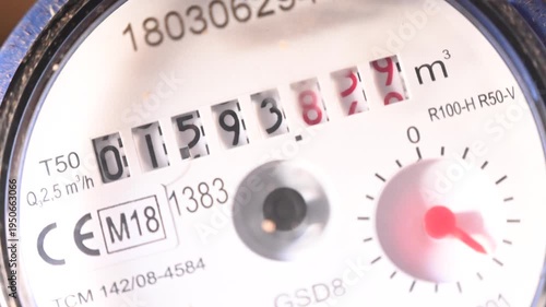 Close-up video of a domestic water meter in operation. Red indicator needles and small rotating dials show real time water consumption. Concept of utility measurement, resource management