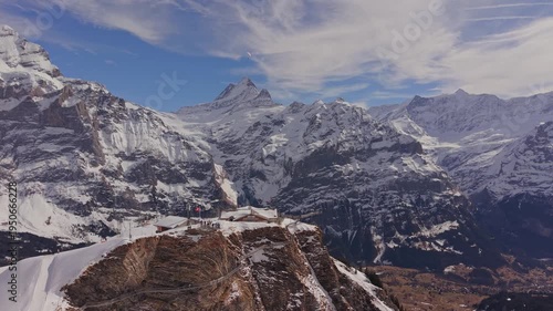 Aerial view of the summit station Grindelwald First, surrounded by massive snowy mountains.