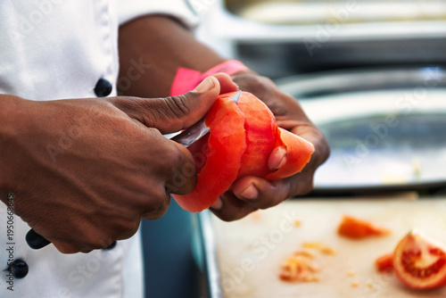 Foto African Chef Peeling a Fresh Tomato with a Paring Knife in a Professional Kitche