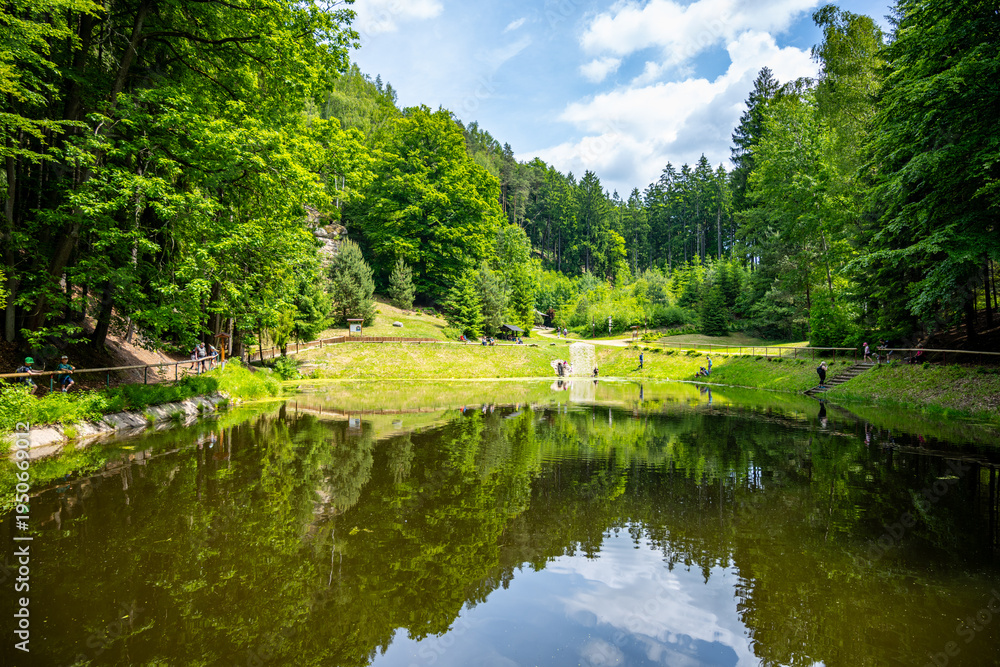Obraz premium Visitors enjoy the Pelisek water reservoir located near Prachovske sandstone rocks in Czechia. This spot features green trees, clear water, and rocky landscapes.