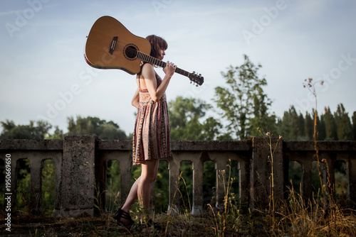 Young Woman with Acoustic Guitar Standing Outdoors at Sunset