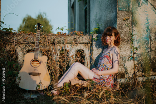 Young Woman Sitting Outdoors with Acoustic Guitar at Sunset