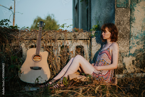 Young Woman Sitting Outdoors with Acoustic Guitar at Sunset