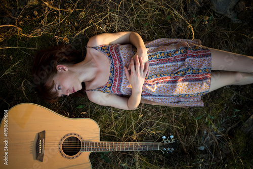 Young Woman Lying on Grass Next to Acoustic Guitar