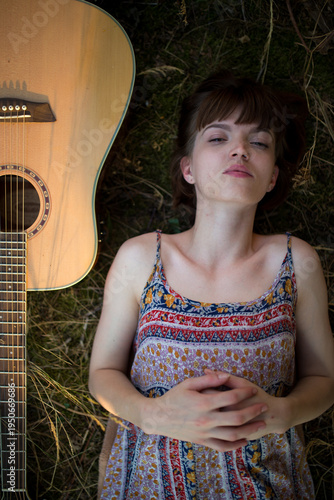 Young Woman Lying on Grass Next to Acoustic Guitar