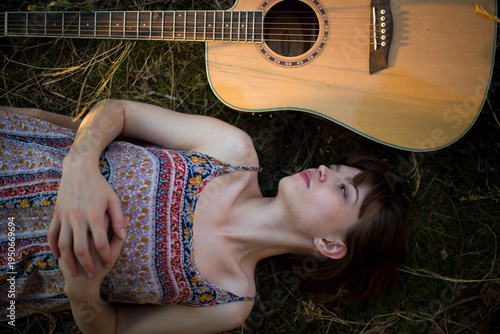 Young Woman Lying on Grass Next to Acoustic Guitar