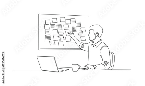 Man writing on sticky notes on a bulletin board with a laptop and coffee nearby